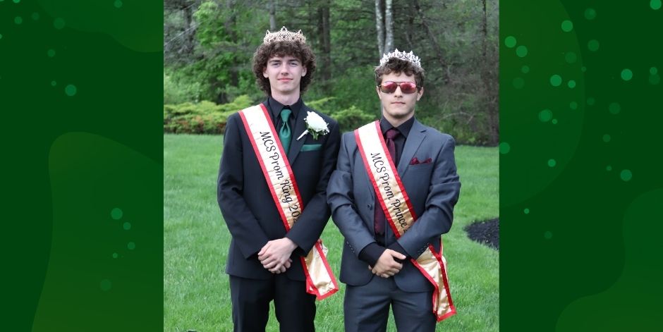 Two teens in formal clothes, crowns and prom sashes.