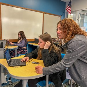 A teacher leaning over a student using a laptop.