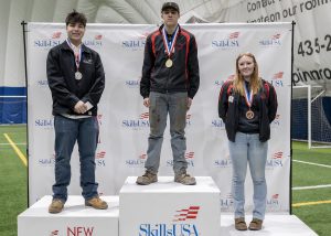 Three teens, wearing medals and Skills USA jackets stand at podium
