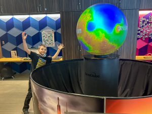Elementary student gestures to show how big a giant globe is in a science center.
