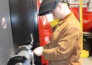 Teen grinds metal. He is wearing a welding helmet.