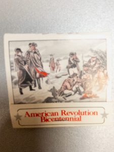 Small commemorative matchbox featuring an illustration of figures in Colonial-era clothing gathered outdoors during winter. The card includes the words “American Revolution Bicentennial” in red lettering at the bottom.
