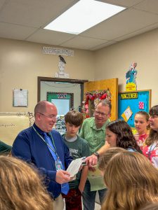 Superintendent Mark Place stands with members of the Class of 2038 and teacher Terry Burton as they examine papers and photographs removed from a time capsule opened at Middleburgh Elementary School.
