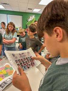 A member of the Class of 2038 holds a preserved class photograph from Middleburgh Elementary School while classmates gather around a table displaying other time capsule items.
