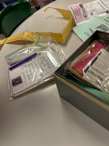 Items removed from a time capsule are spread across a classroom table, including documents, preserved papers, plastic storage bags, newspaper clippings and a metal box used to store the collection.