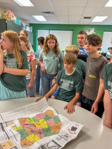 Members of the Class of 2038 gather around a classroom table to examine a map preserved in a time capsule. Colorful notes mark local businesses and landmarks throughout the Middleburgh area.