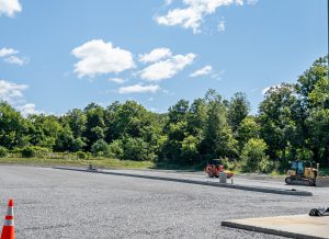 Construction equipment on a newly graded parking lot near a tree line.