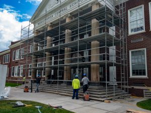 Scaffolding surrounds the front entrance of Middleburgh Central School as construction crews work on restoration and improvement projects around the building's large entrance columns. The historic brick school building and columned facade are visible behind the temporary structure.
