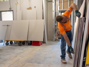 Man measures dry wall on interior construction site.
