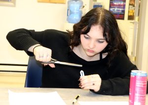 A Capital Region BOCES EMT student uses scissors to modify a component of a respiratory system model during a classroom lesson. The activity uses balloons, straws and a plastic bottle to demonstrate how the lungs function.